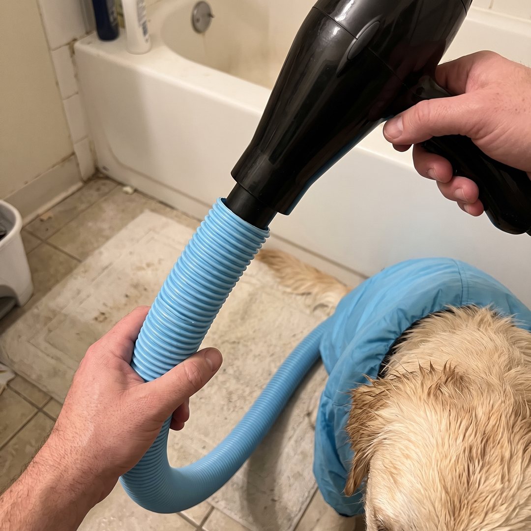 A hand pushing a household hair dryer nozzle into the FluffDry hose